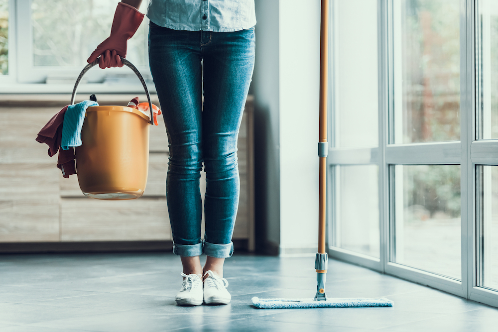 A young woman holds a bucket of cleaning supplies 