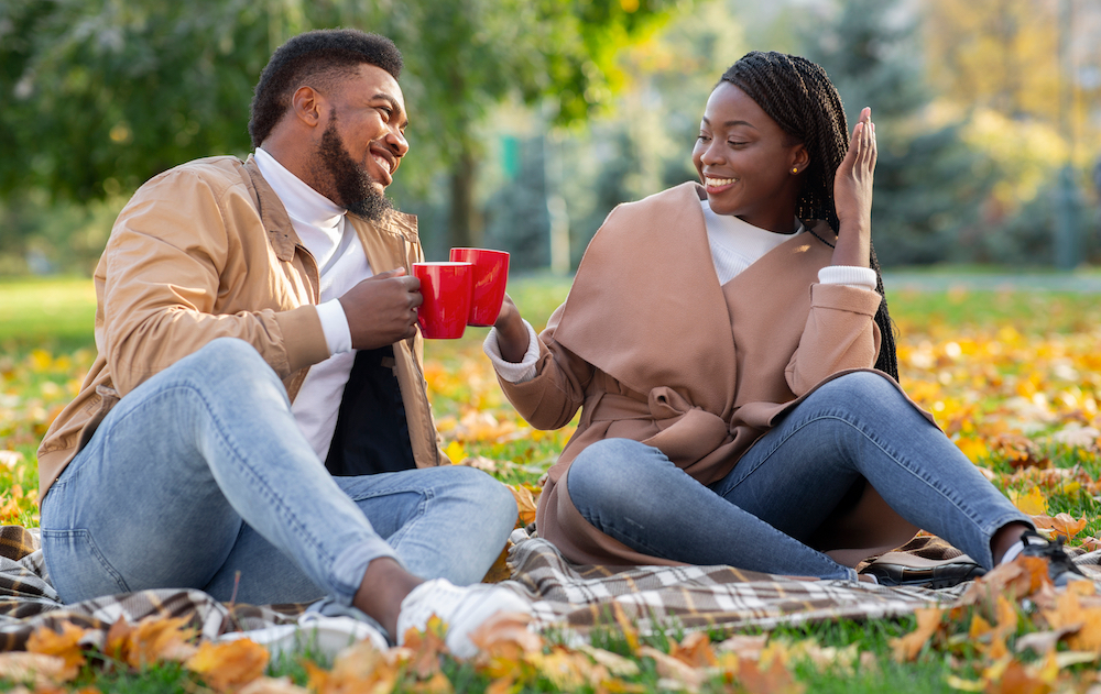 A couple enjoys drinking coffee while on a fall picnic at the park
