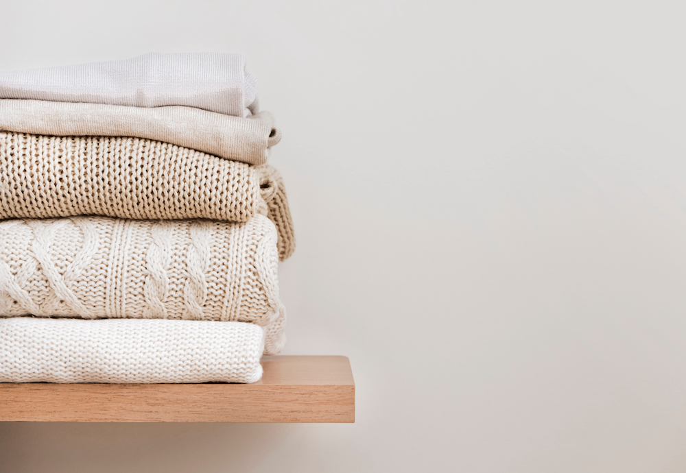 A stack of sweaters folded on a shelf in the closet
