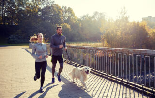 A young couple jogs through a park with their dog
