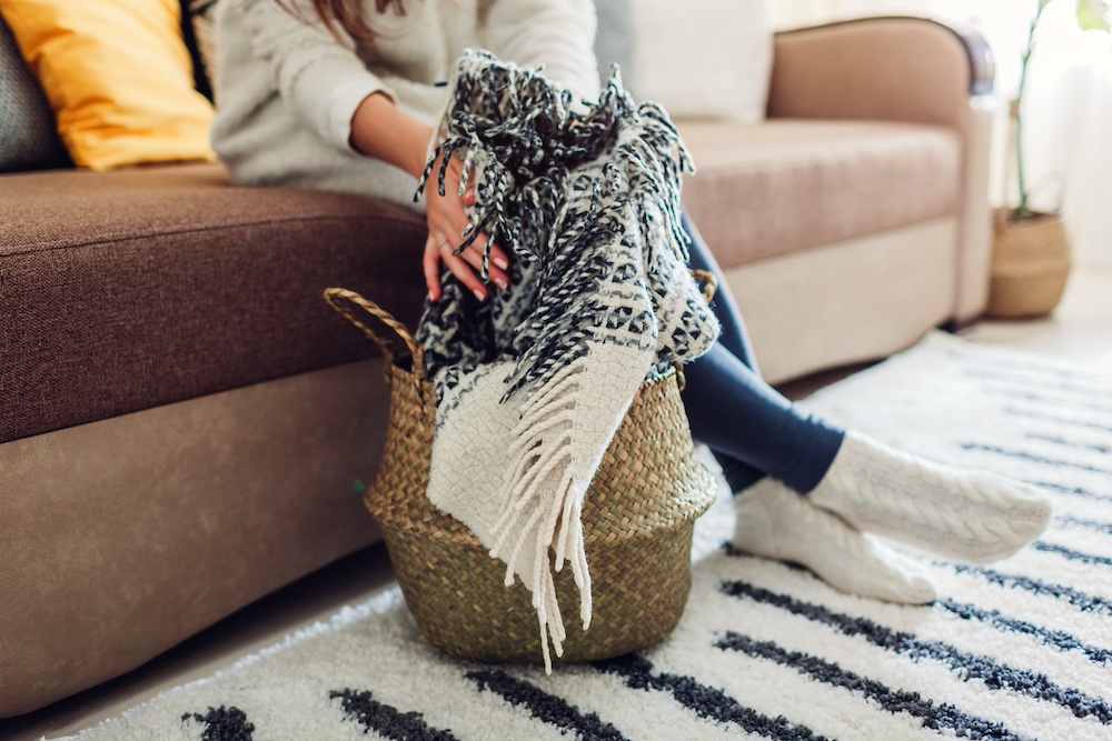 A woman storing a throw blanket in a woven tote